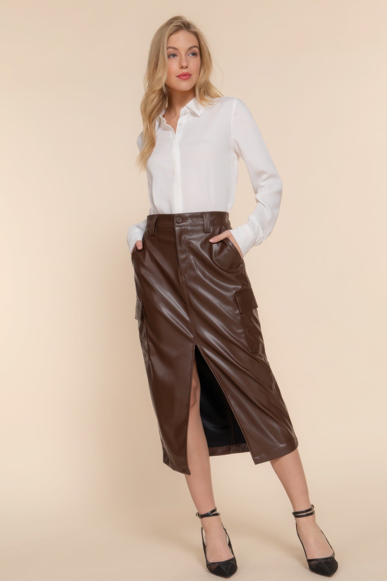 Woman wearing a faux leather midi cargo skirt with a white blouse, showcasing sleek style and cargo pockets.