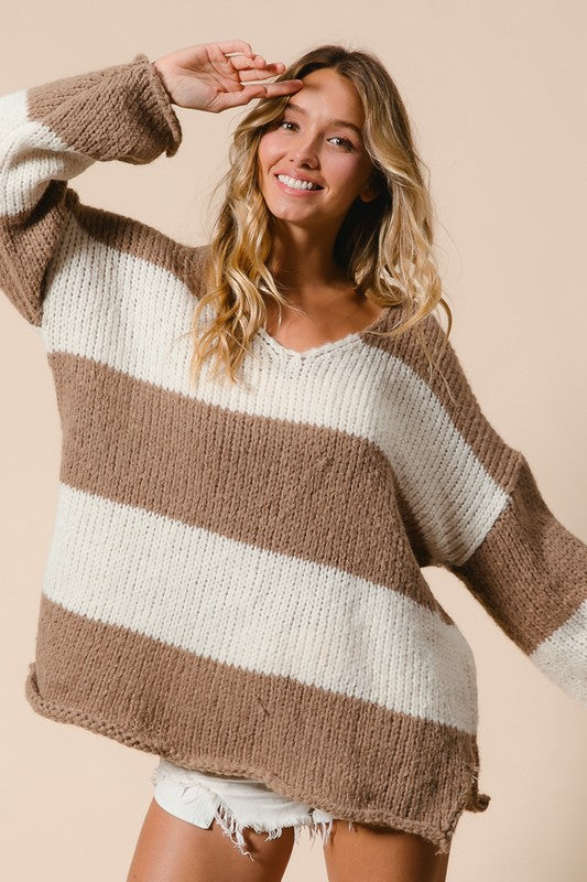 Woman wearing a cozy BiBi slit striped V-neck dropped shoulder sweater in beige and white for a stylish, relaxed look.