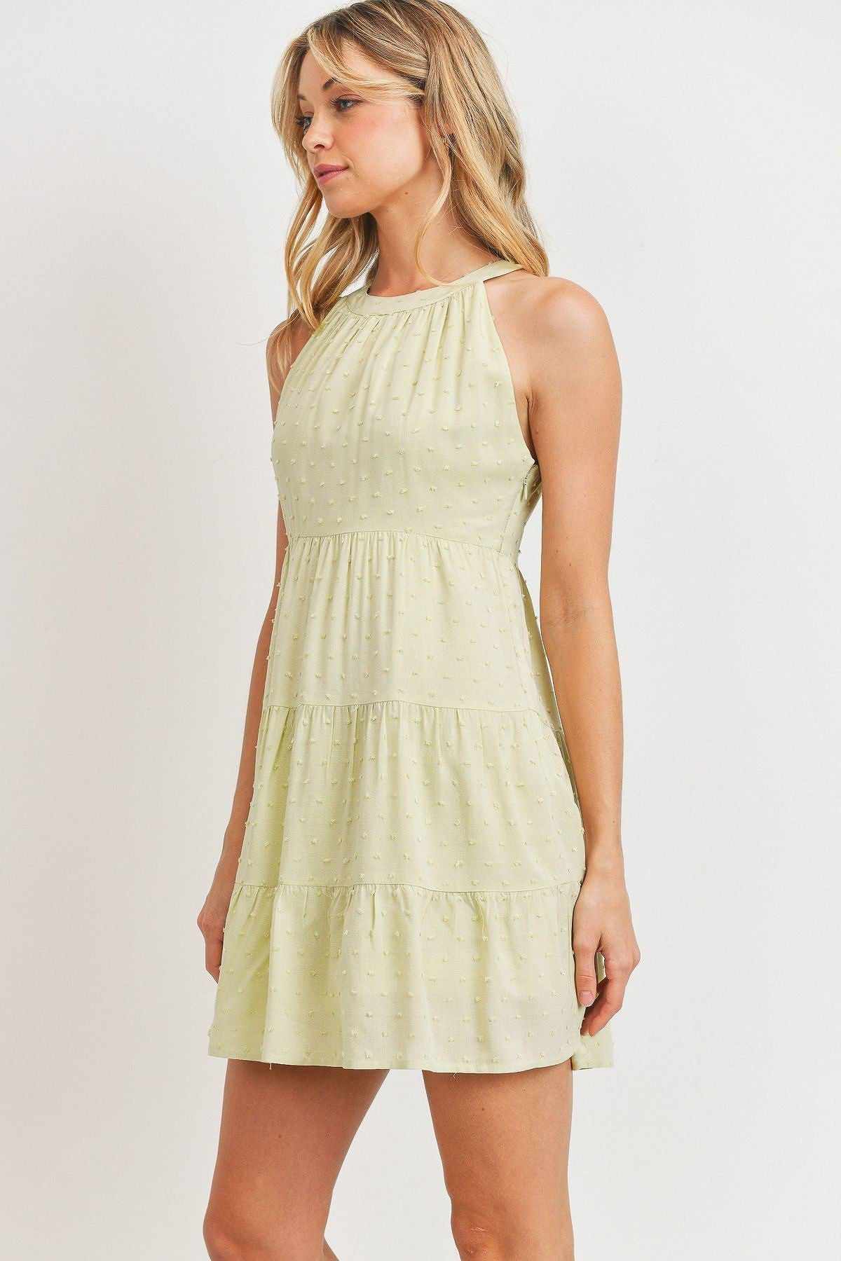 Woman wearing sage sleeveless round-neck dress with woven pompom textures and mini hemline.