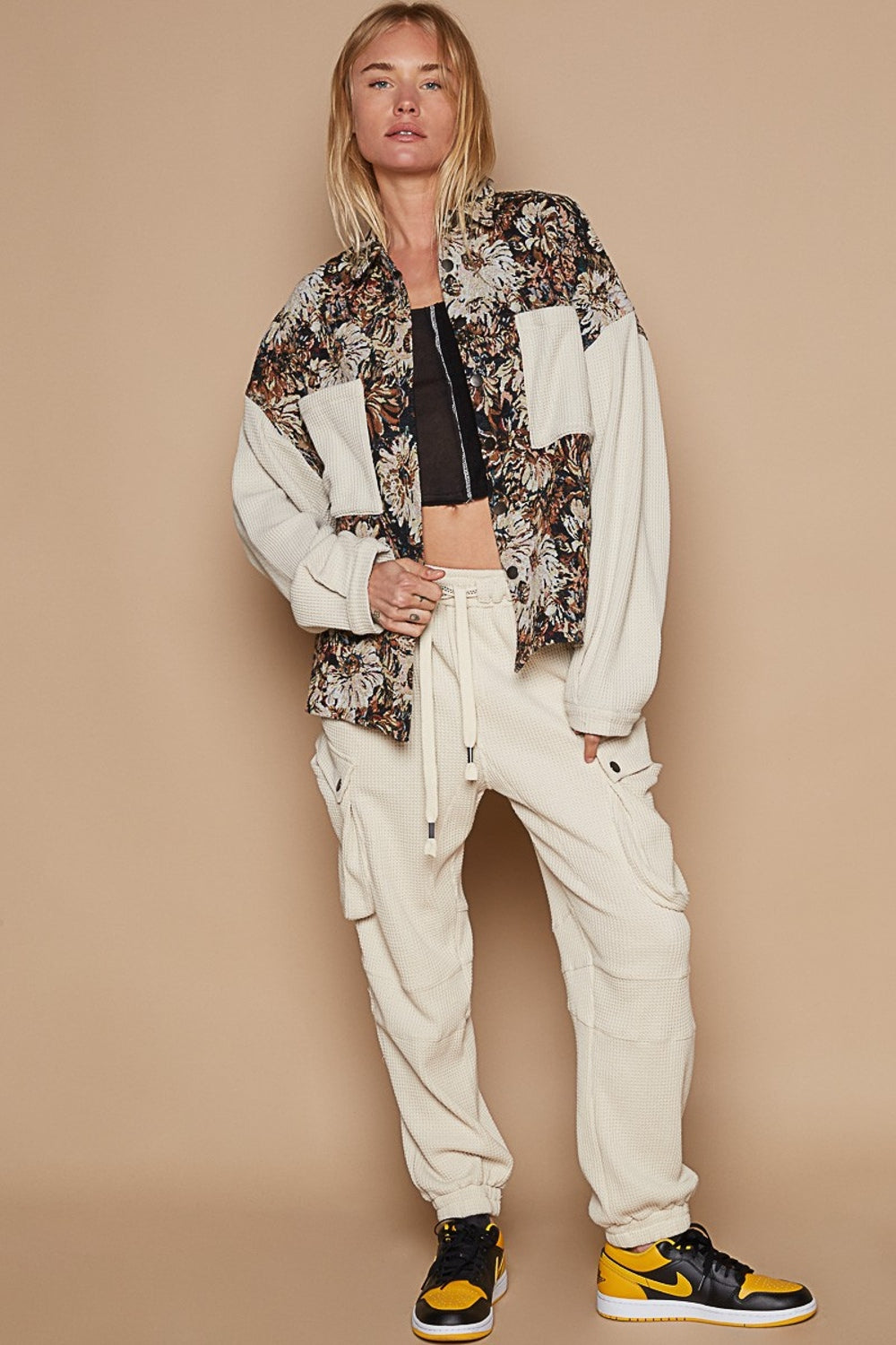 Model wearing a contrast floral jacquard jacket with beige cargo pants and yellow-black sneakers against a neutral background.