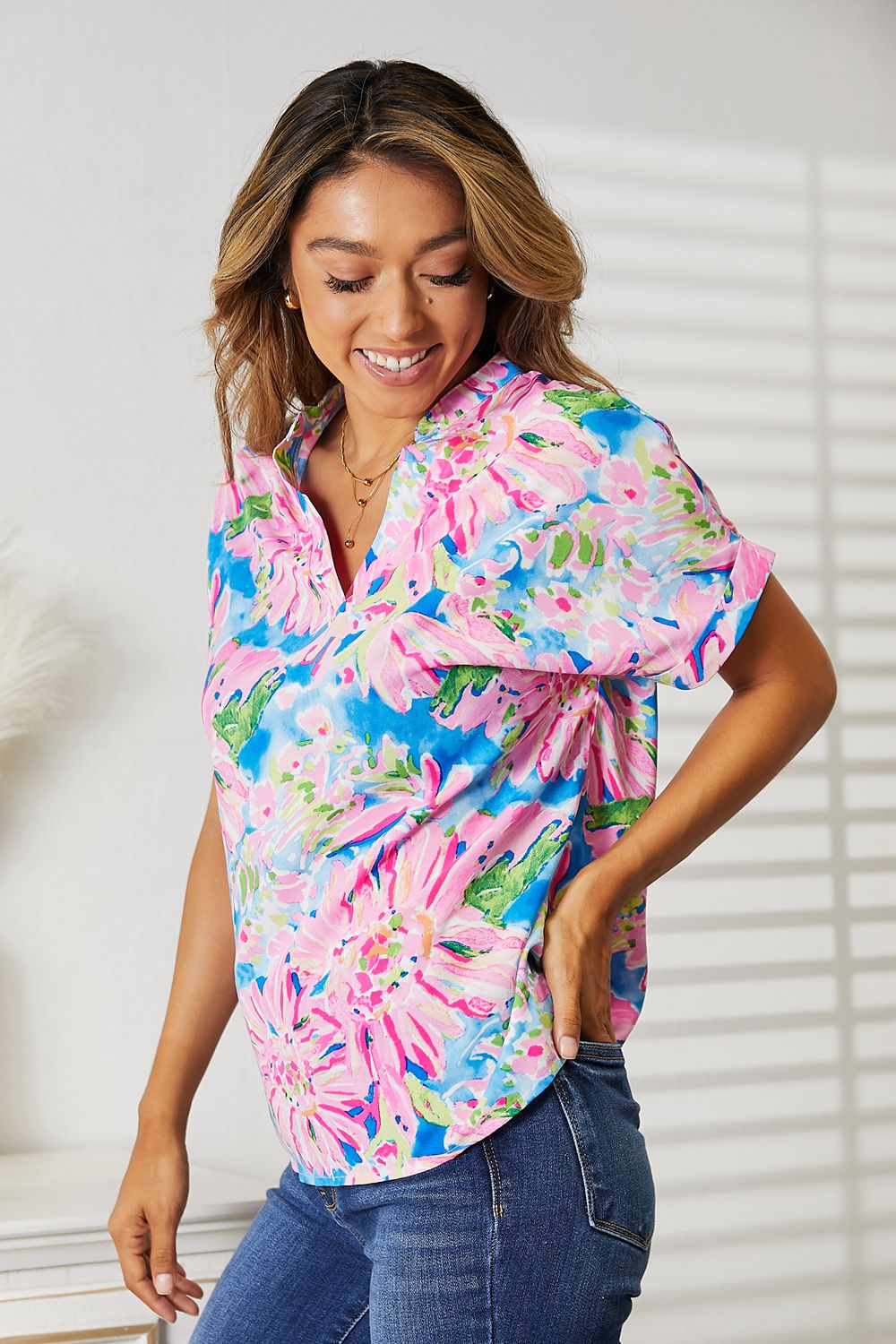 Woman wearing a Double Take floral notched neck short sleeve top with vibrant floral print, paired with blue jeans for a stylish look.