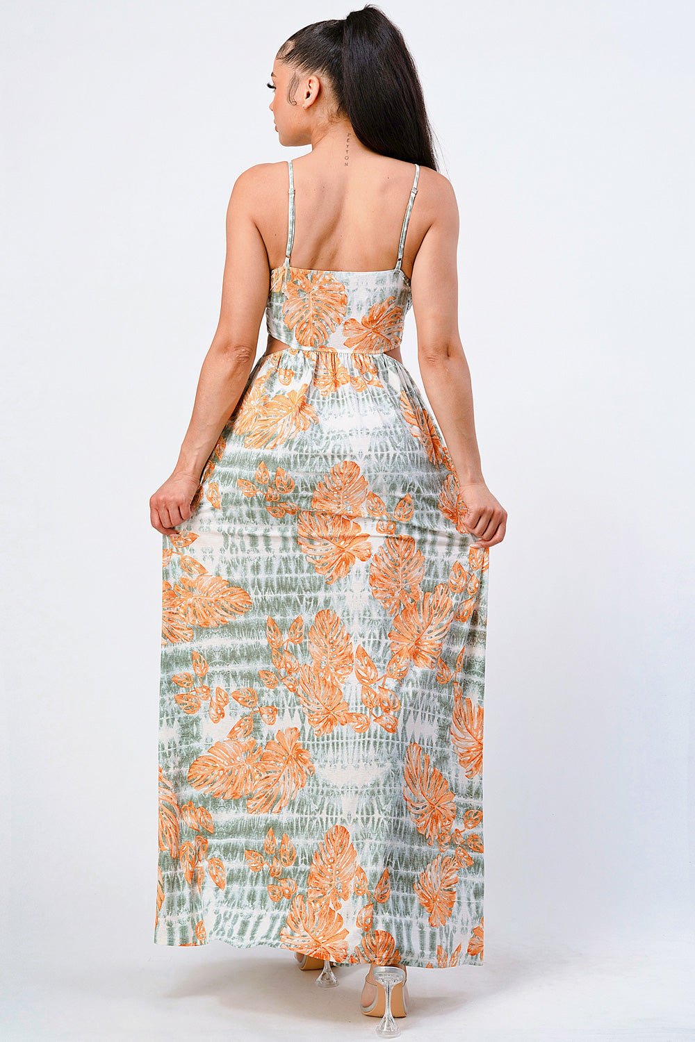 Woman wearing a floral printed side slit maxi dress with orange and green patterns, showcasing back view with spaghetti straps.