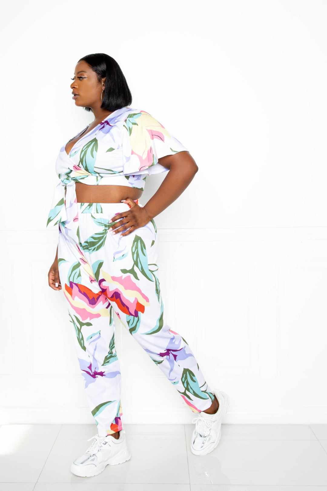 Plus-size model wearing a colorful floral jogger and top set in polyester-spandex blend, showcasing a vibrant multi/white design.