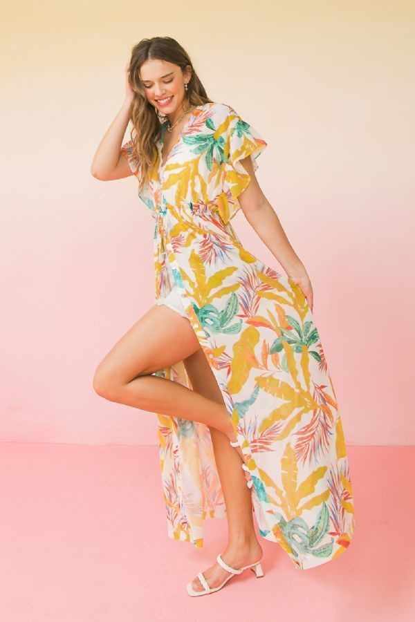 Woman wearing a colorful printed woven maxi cover up with ruffled sleeves and open front tie, standing against a pastel background.