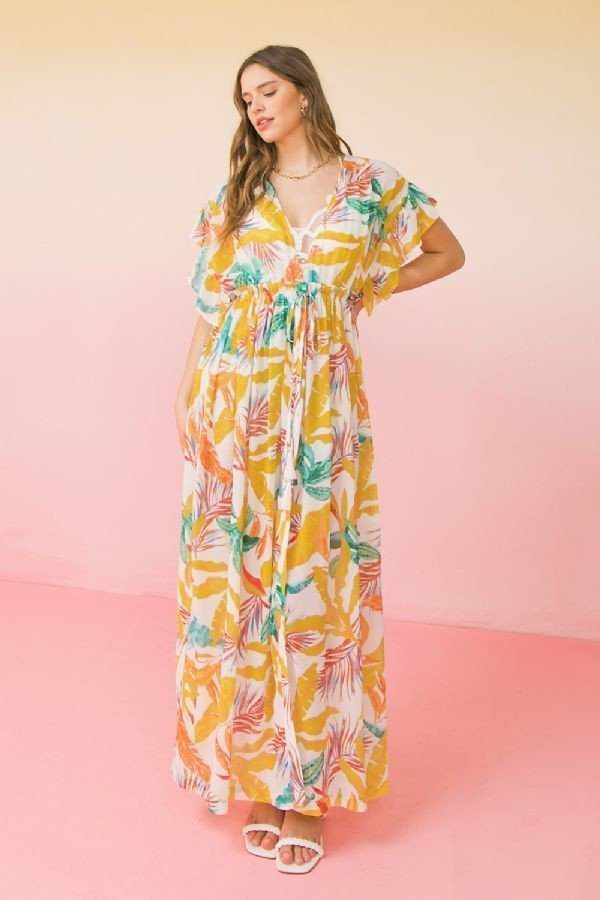 Woman wearing printed woven maxi cover up with open front tie and ruffled sleeves, colorful leaf pattern on ivory fabric.