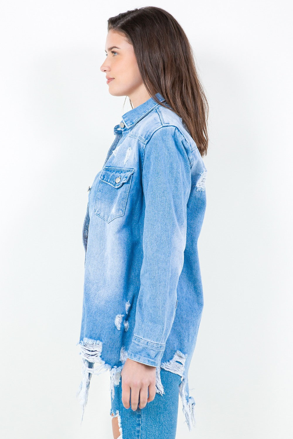 Woman wearing frayed hem distressed denim shirt jacket, showcasing washed blue style with edgy details for casual layering.