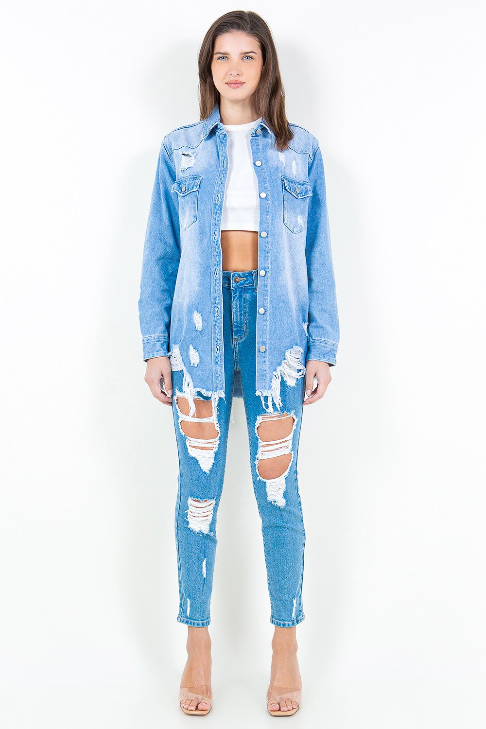 Woman wearing a frayed hem distressed denim shirt jacket with ripped jeans, showcasing a trendy and edgy casual style.