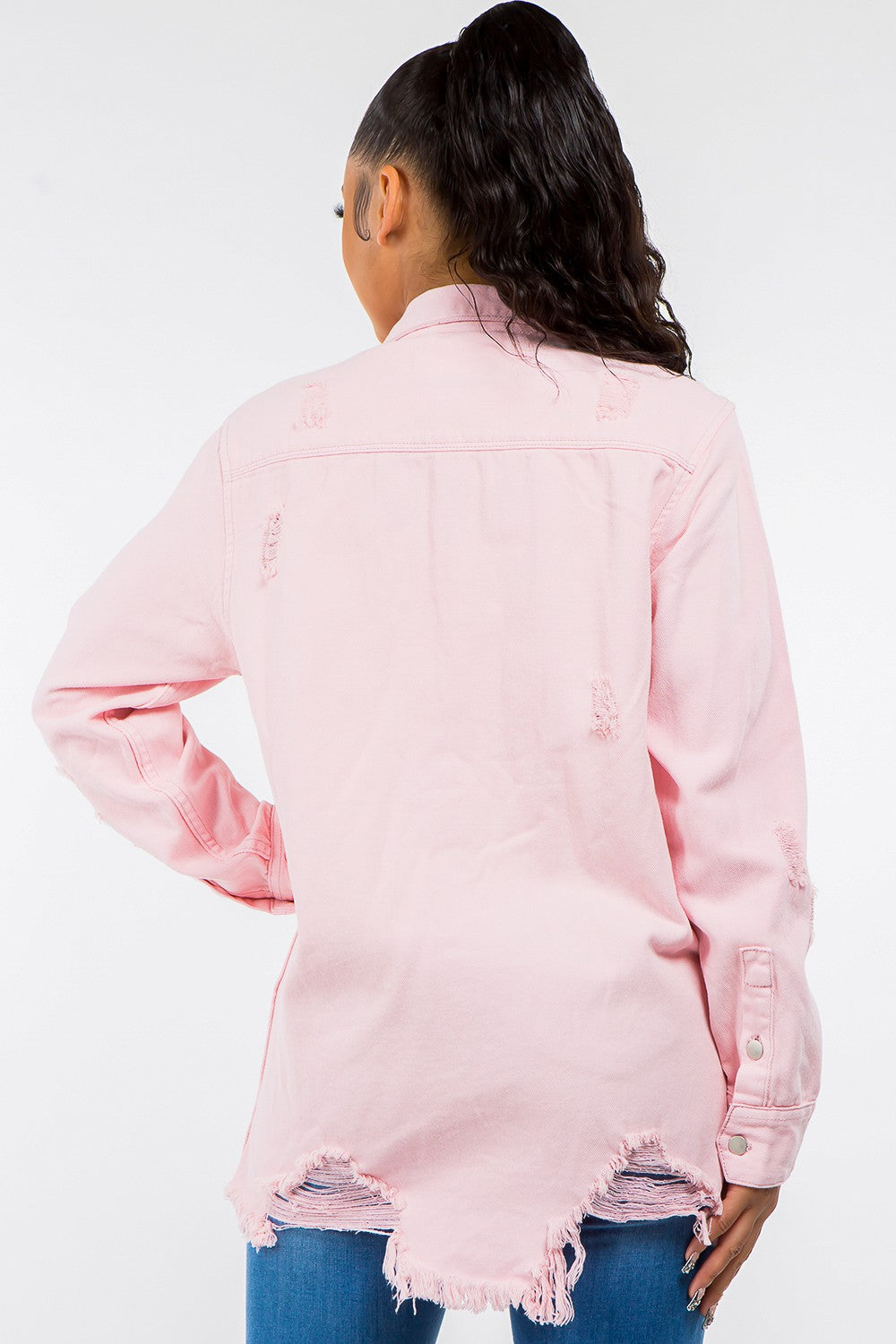 Woman wearing a pink frayed hem distressed denim jacket, showing back view with raw detailing, over blue jeans.