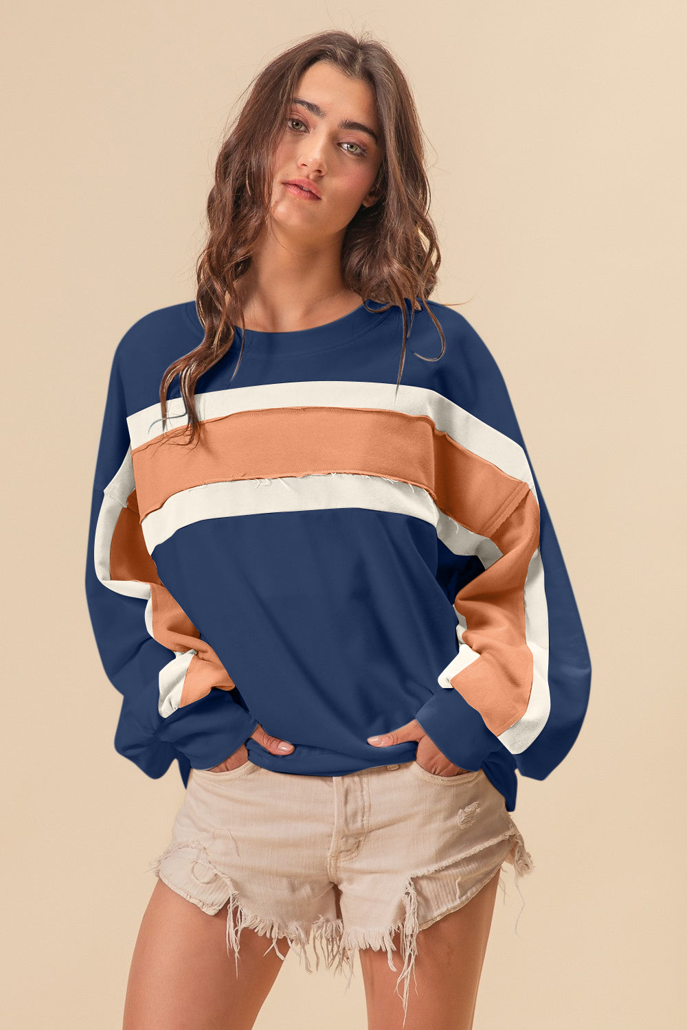 Woman wearing French Terry Color Block Cut Edge Detail Sweatshirt with navy, beige, and white stripes and tan shorts.