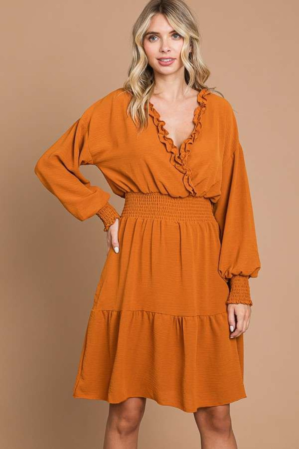 Woman wearing orange frill smocked lantern sleeve mini dress with highly stretchy material, featuring a V-neck and cinched waist.