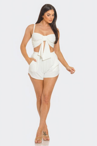 Woman wearing white oversized tie top and shorts set with elastic waistband and side pockets, featuring a chic front bow design.