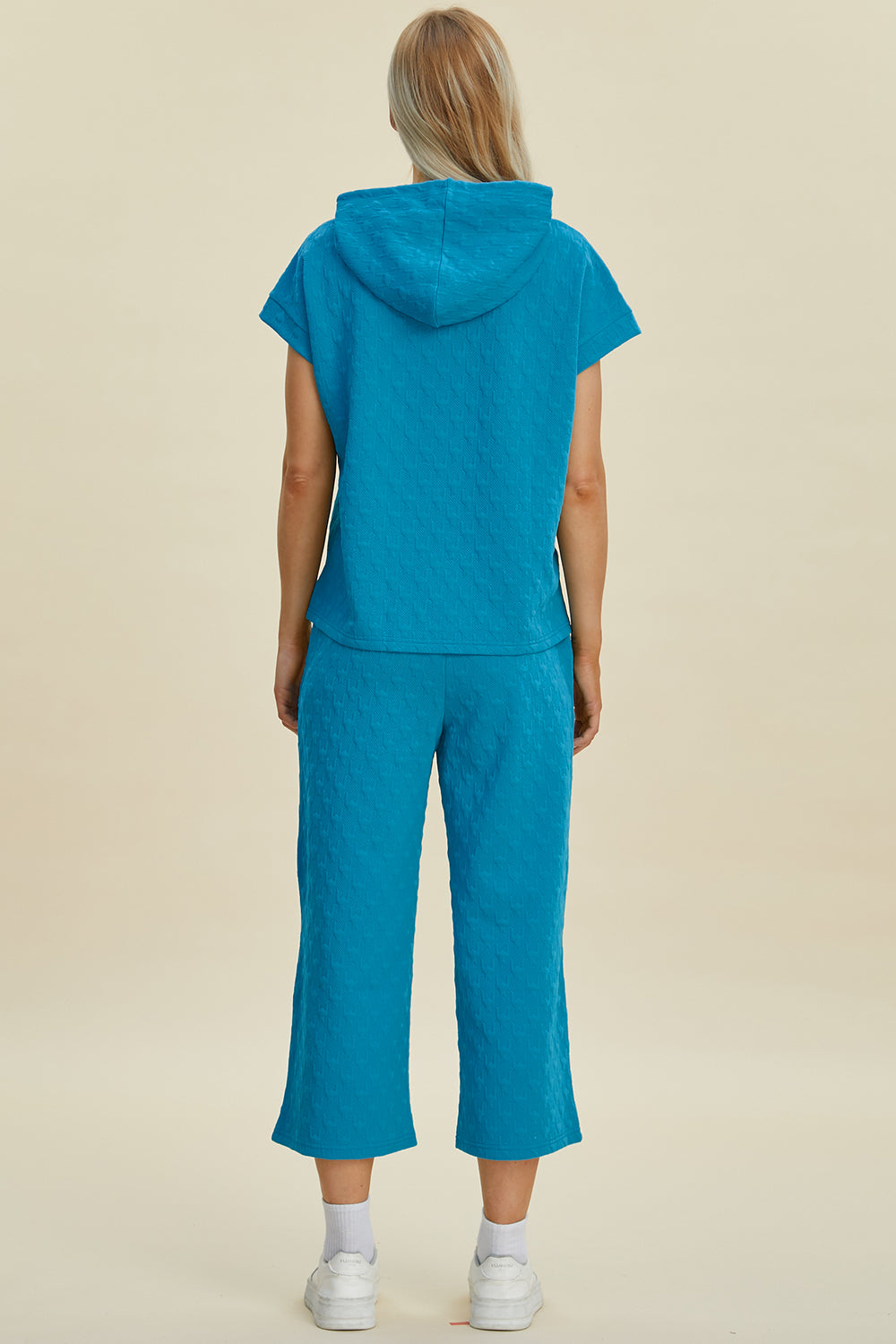 Woman wearing blue short sleeve hoodie and pocketed pants set, featuring drawstring and slight stretch, made of polyester and spandex.