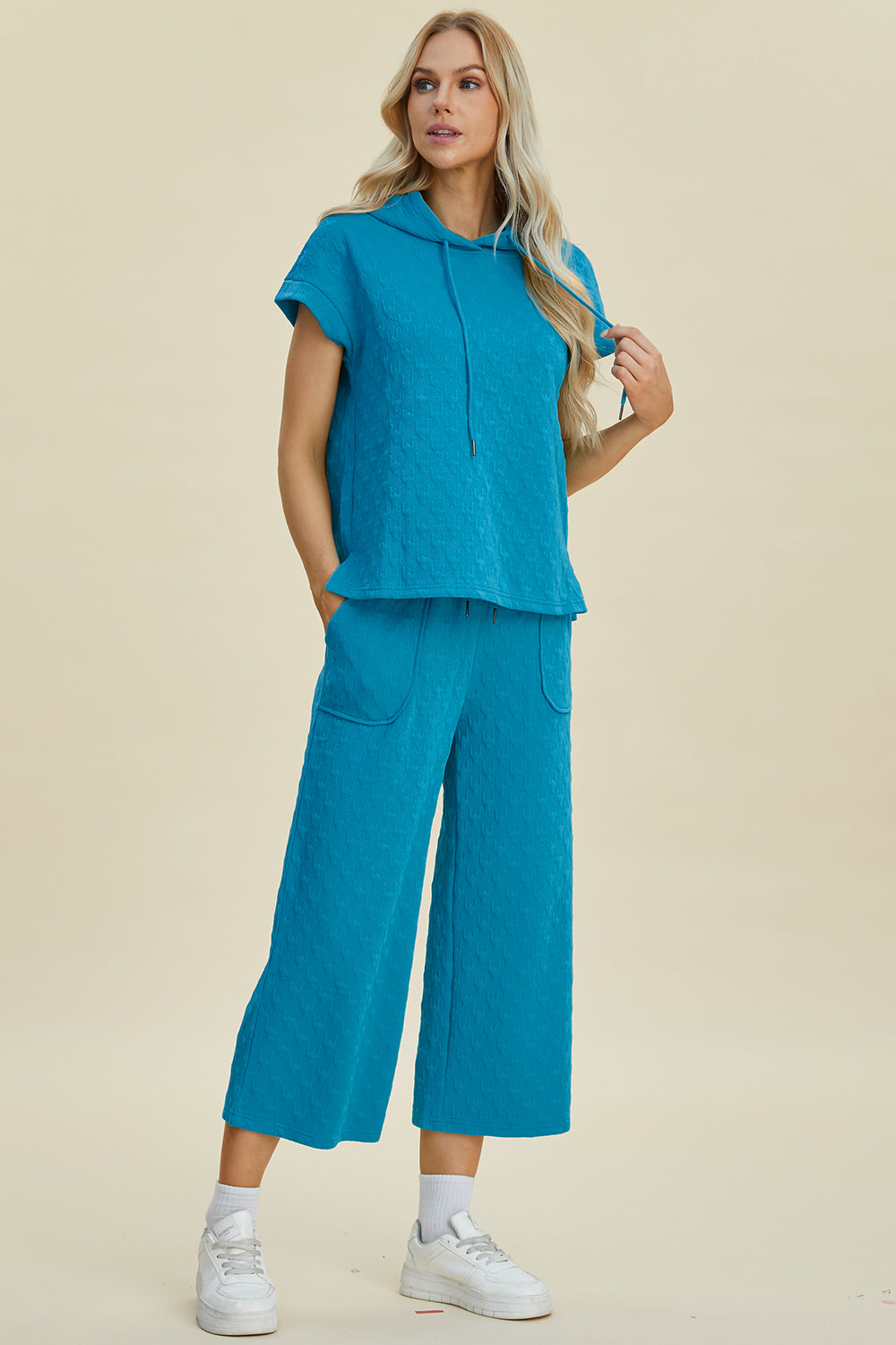 Woman wearing a blue full size texture short sleeve hoodie and pocketed pants set with drawstring, made of 95% polyester, 5% spandex.