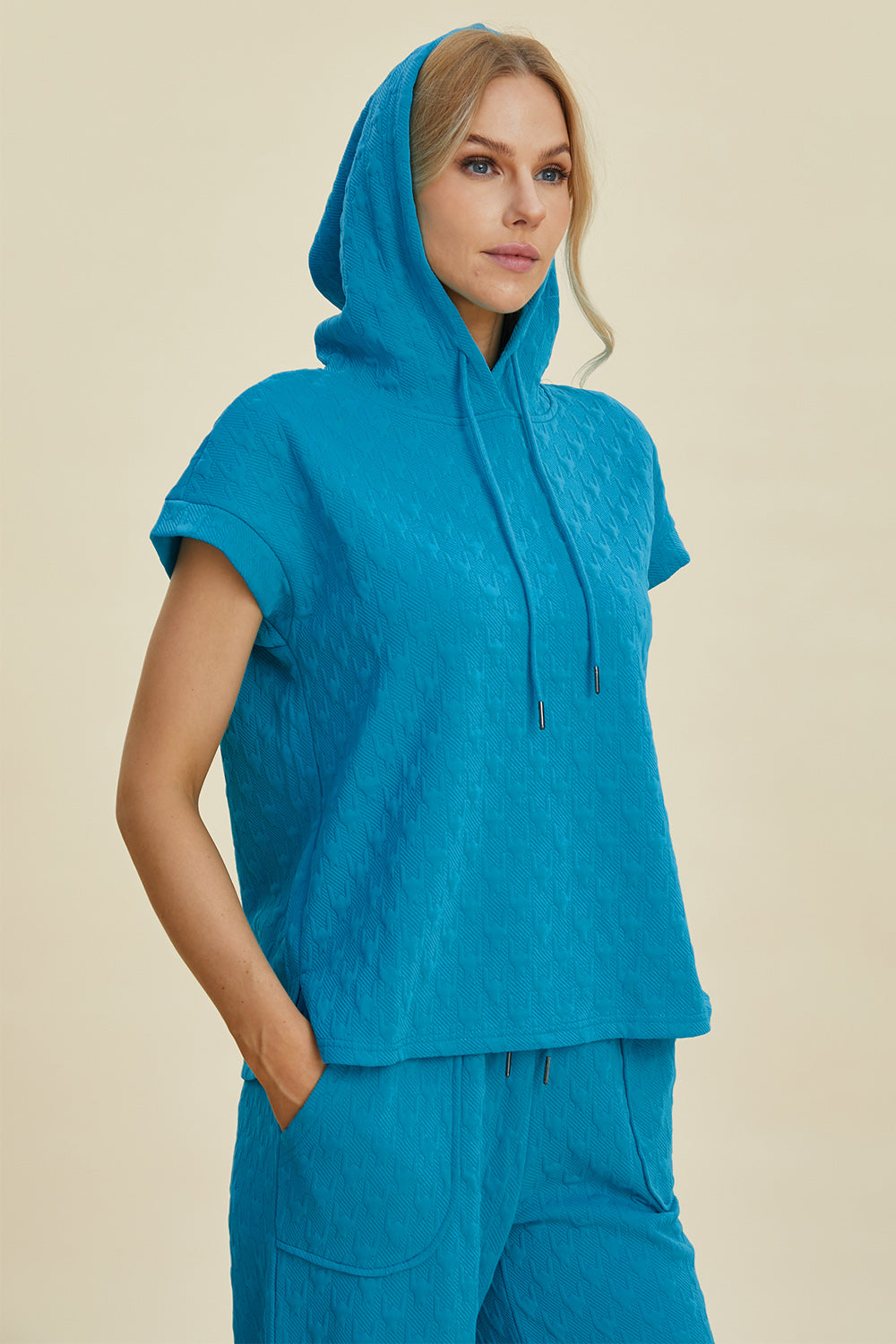 Woman wearing a blue short sleeve hoodie and pocketed pants set with drawstring, slightly stretchy polyester-spandex blend.