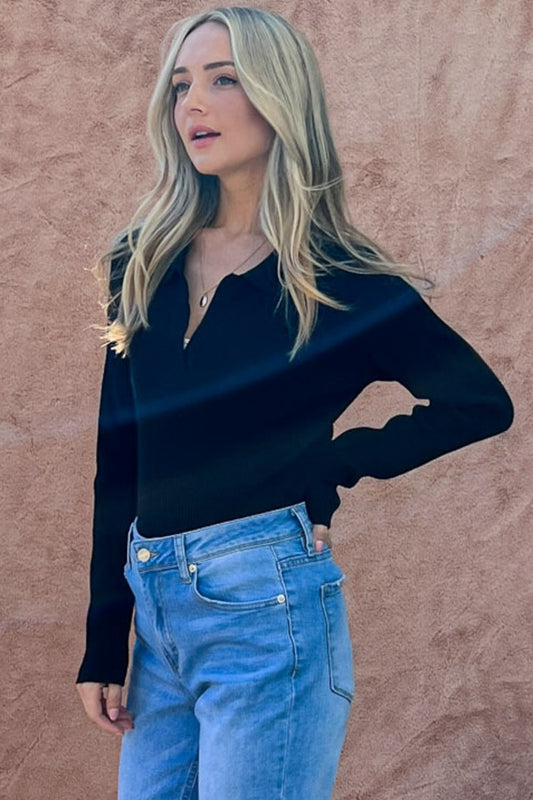 Woman wearing The Why Full Size Johnny Collar Long Sleeve Ribbed Bodysuit in black with jeans against a textured background.