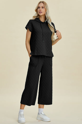 Woman wearing full-size short sleeve hoodie and pocketed pants set, featuring drawstring and slightly stretchy material, in black.