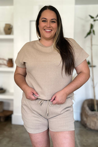Woman wearing beige full size texture short sleeve top and shorts set with pockets and drawstring, made of polyester and elastane.