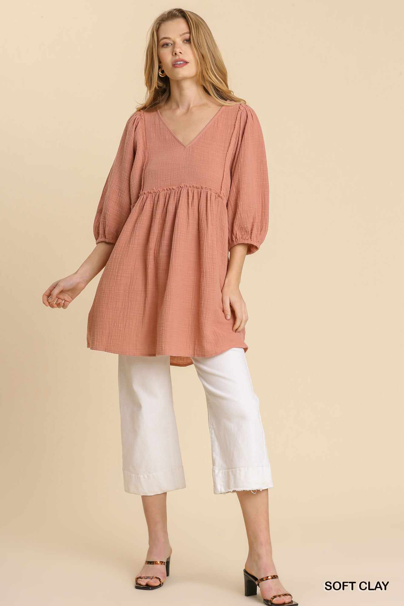 Woman wearing a soft clay gauze slub V-neck tunic dress with frayed edge detail, over white cropped pants.