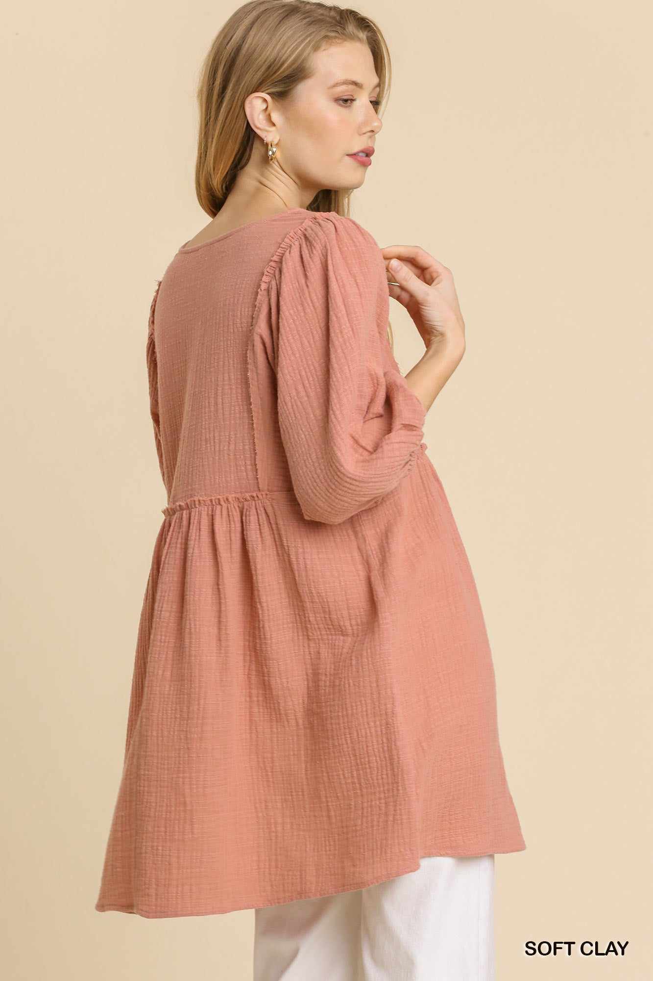 Woman wearing soft clay gauze slub V-neck tunic dress with frayed edge detail and ruched back, styled with white pants.