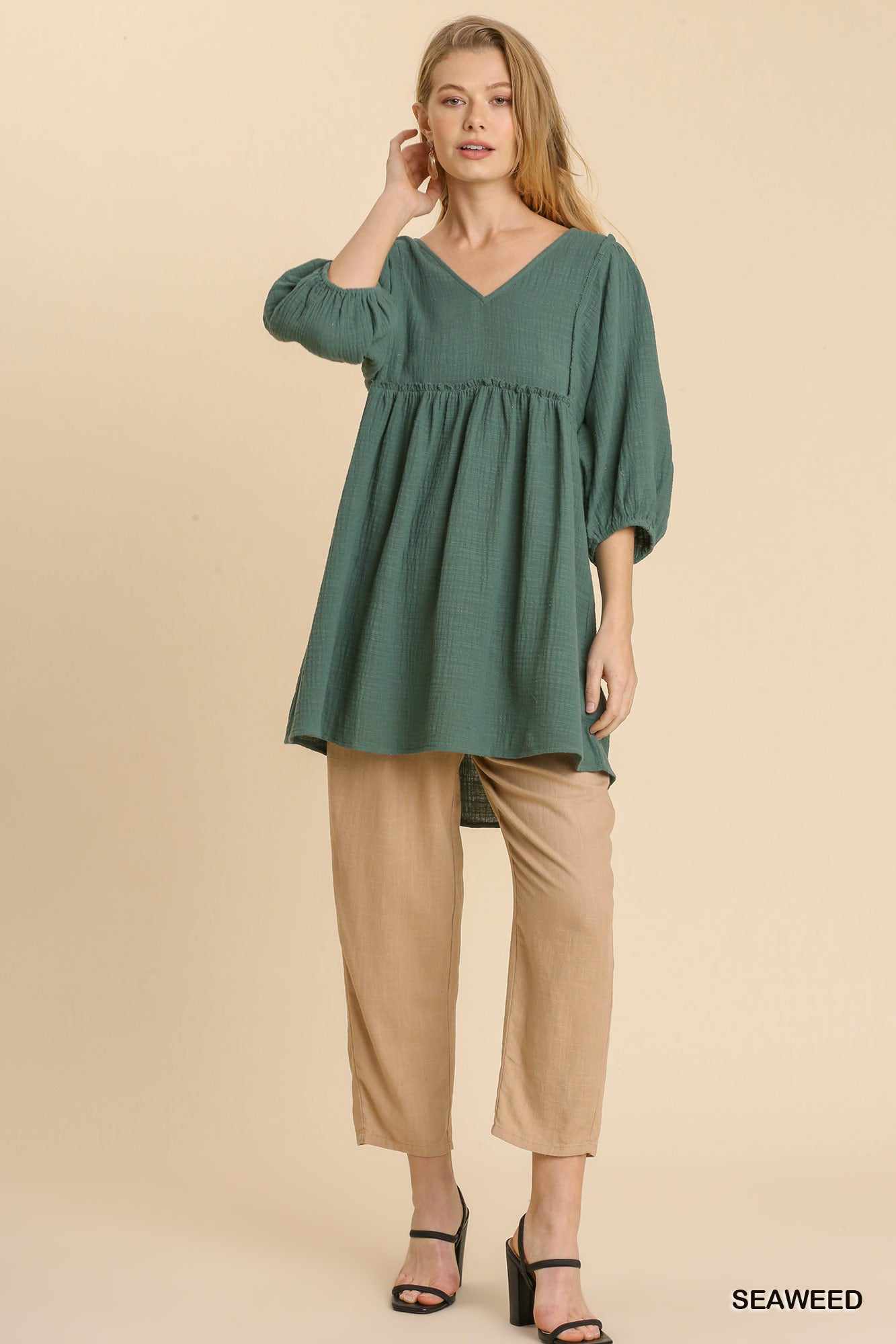 Woman wearing green Gauze Slub V-neck Frayed Edge Tunic Dress with beige pants, showcasing relaxed fit and casual style.