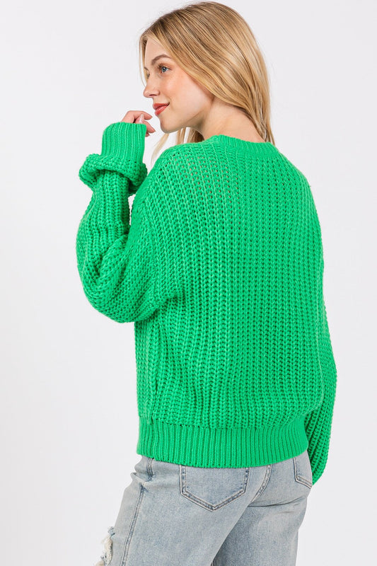 Woman wearing a green round neck drop shoulder sweater made of 100% acrylic, showcasing basic style with slight stretch.