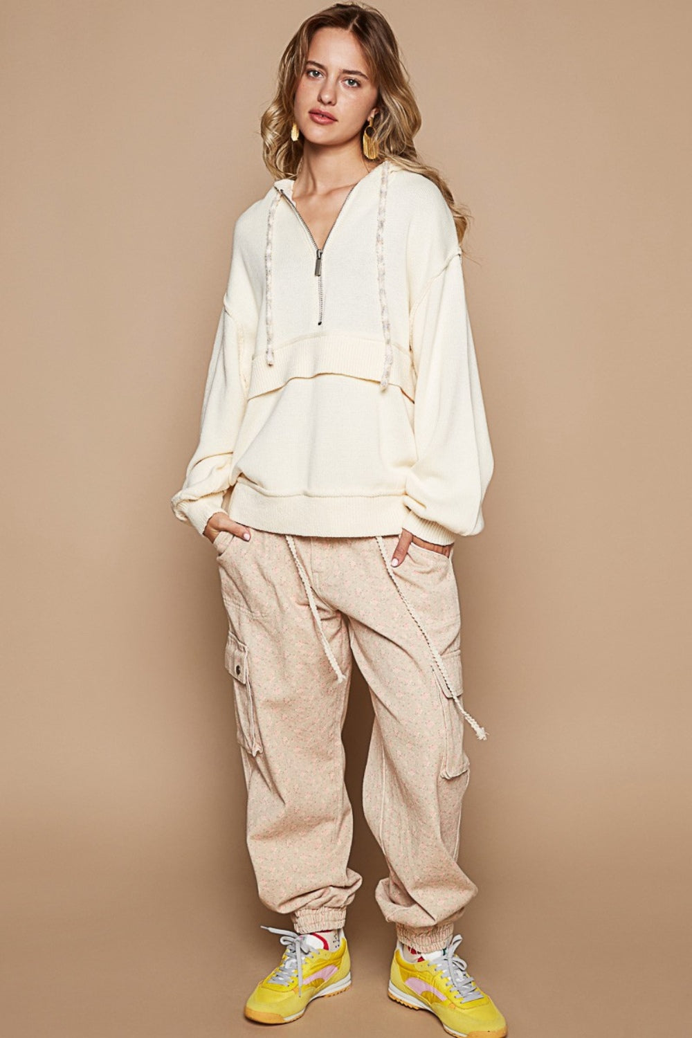 Woman wearing half zip drop shoulder hooded sweater with drawstring and ribbed texture, paired with loose pants and yellow sneakers.