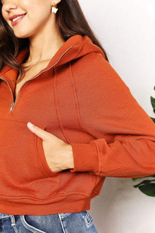 Woman wearing chic, solid orange half-zip long sleeve cropped hoodie with collared neck and raglan sleeves, hands in pockets.