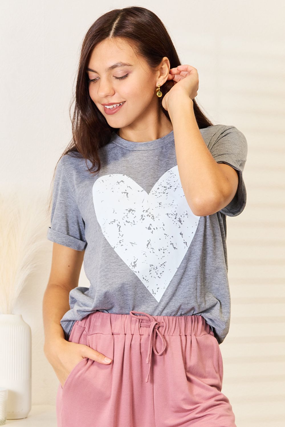 Woman wearing heart graphic cuffed short sleeve T-shirt in gray, paired with pink pants, perfect for casual and dressy styles.