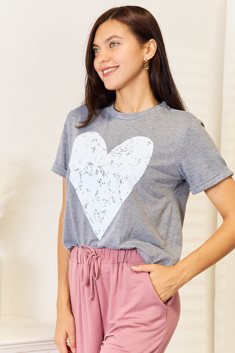 Woman wearing a heart graphic cuffed short sleeve t-shirt in gray with pink pants, showing versatile everyday style.