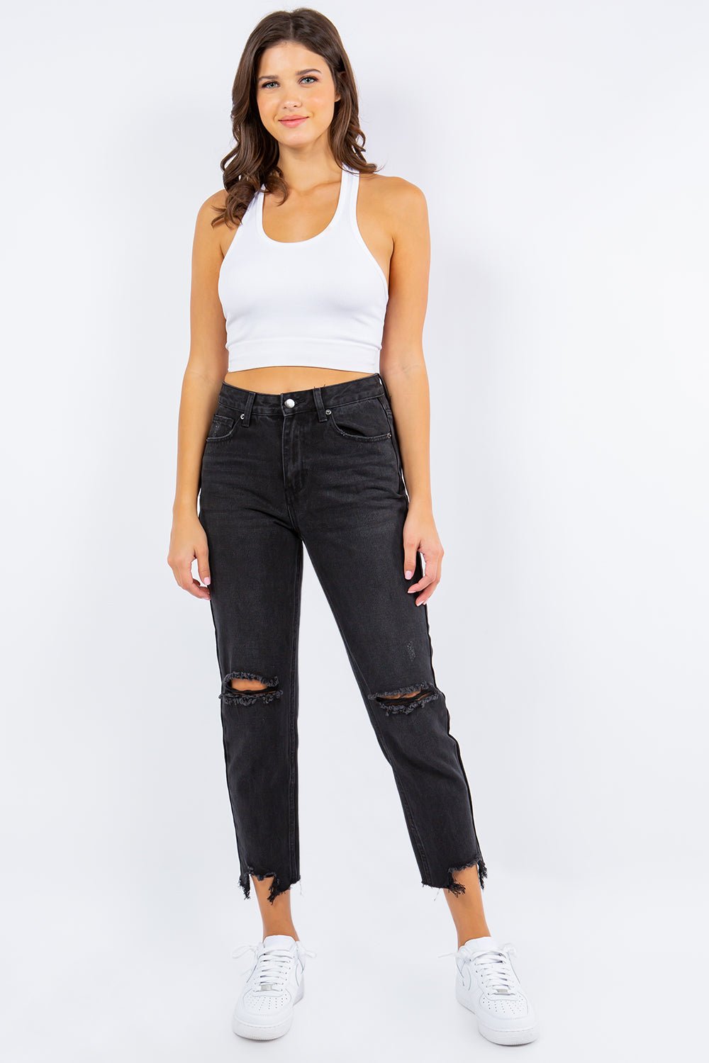 Woman modeling high waist distressed cropped straight jeans with a white tank top and sneakers.