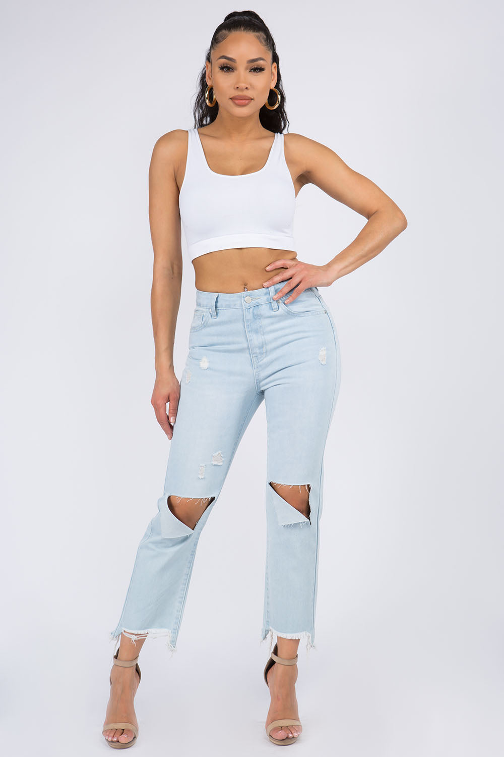 High waist distressed raw hem jeans in light denim, styled with a white tank top and heels, showcasing edgy and trendy fashion.