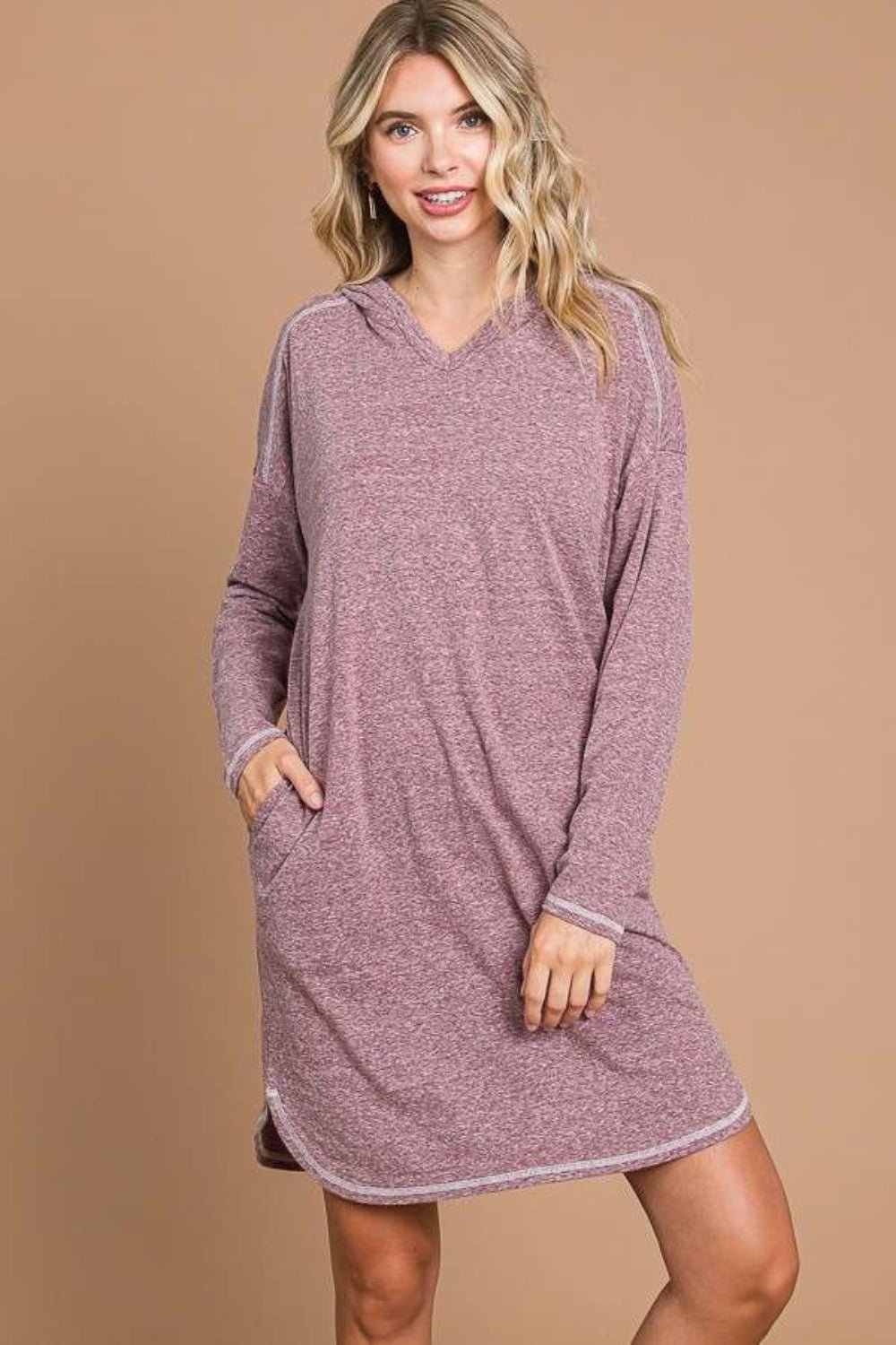 Woman wearing a hooded long sleeve sweater dress in pink, featuring moderate stretch and pockets, made from cotton, polyester, rayon, and spandex.