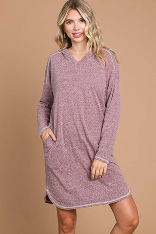Woman wearing a hooded long sleeve sweater dress in pink, featuring moderate stretch and pockets, made from cotton, polyester, rayon, and spandex.