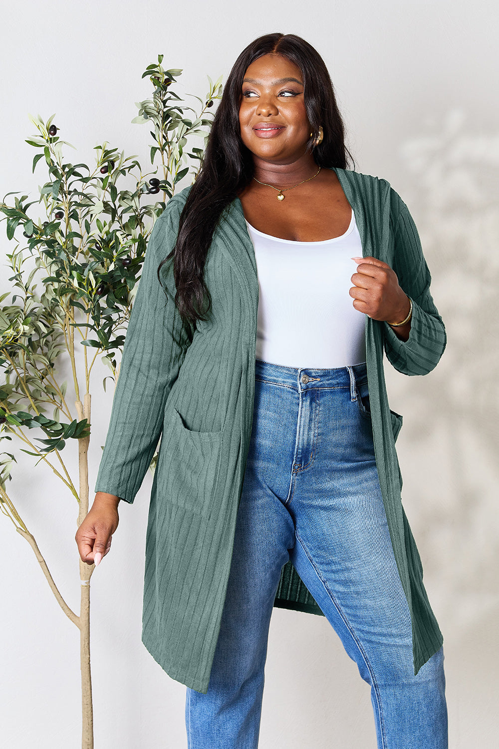 Woman wearing a green hooded sweater cardigan with pockets and slightly stretchy fabric, paired with blue jeans and a white top.