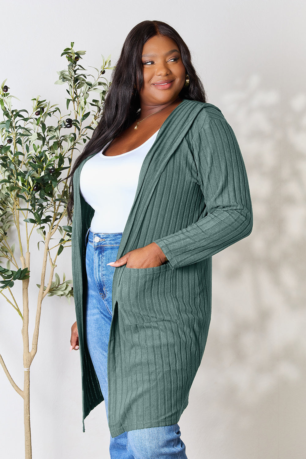 Woman wearing a green hooded sweater cardigan with pockets, paired with a white top and jeans.