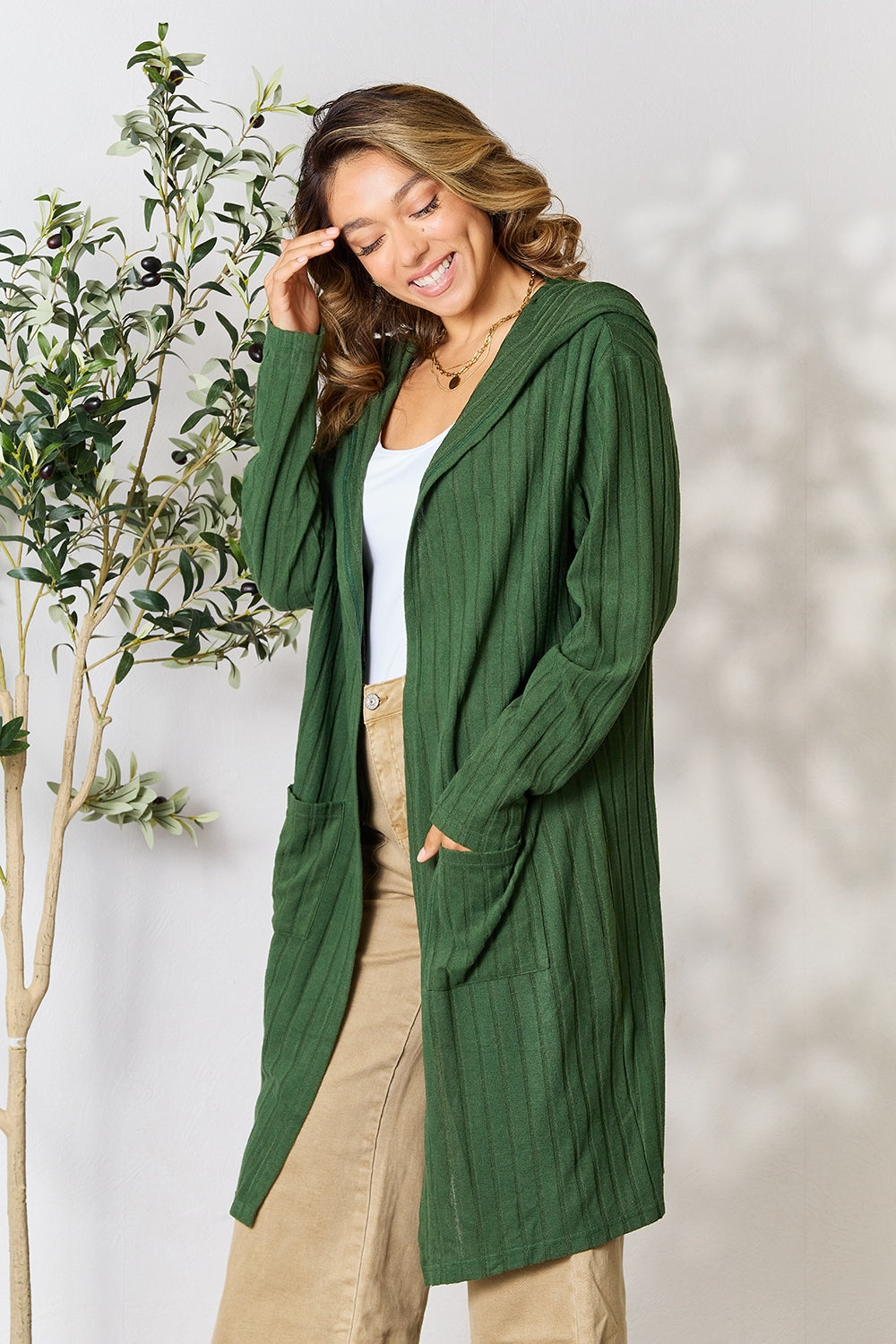 Woman wearing a green hooded sweater cardigan with pockets, slightly stretchy fabric, paired with beige pants.