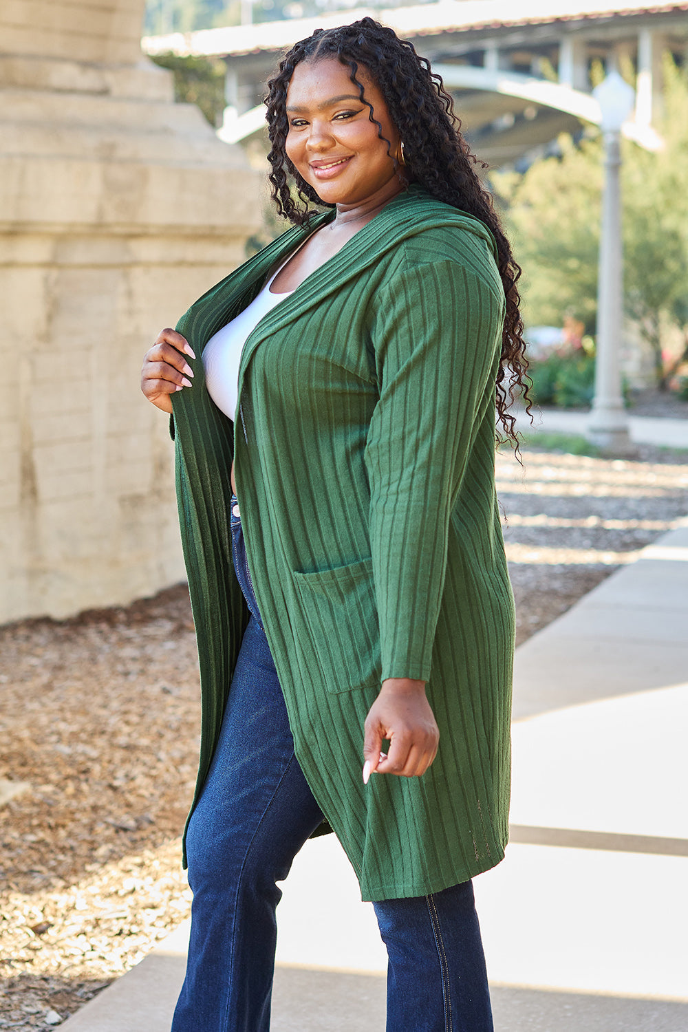 Woman wearing a green hooded sweater cardigan with pockets, styled over a white top and jeans. Perfect for a casual, cozy look.