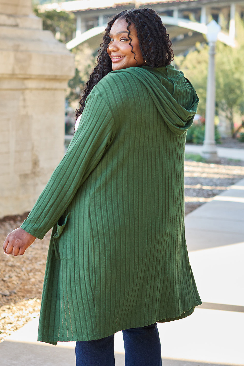 Woman wearing a green hooded sweater cardigan with pockets, slightly stretchy opaque fabric, perfect for casual outings.