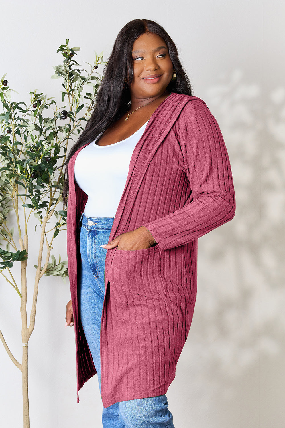 Woman wearing hooded sweater cardigan with pockets, slightly stretchy and opaque, styled with jeans and a white top.