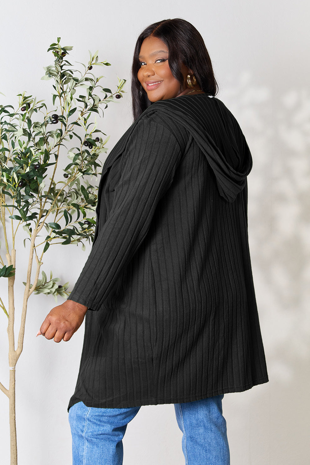 Woman wearing a black hooded sweater cardigan with pockets, slightly stretchy and opaque, styled with jeans.