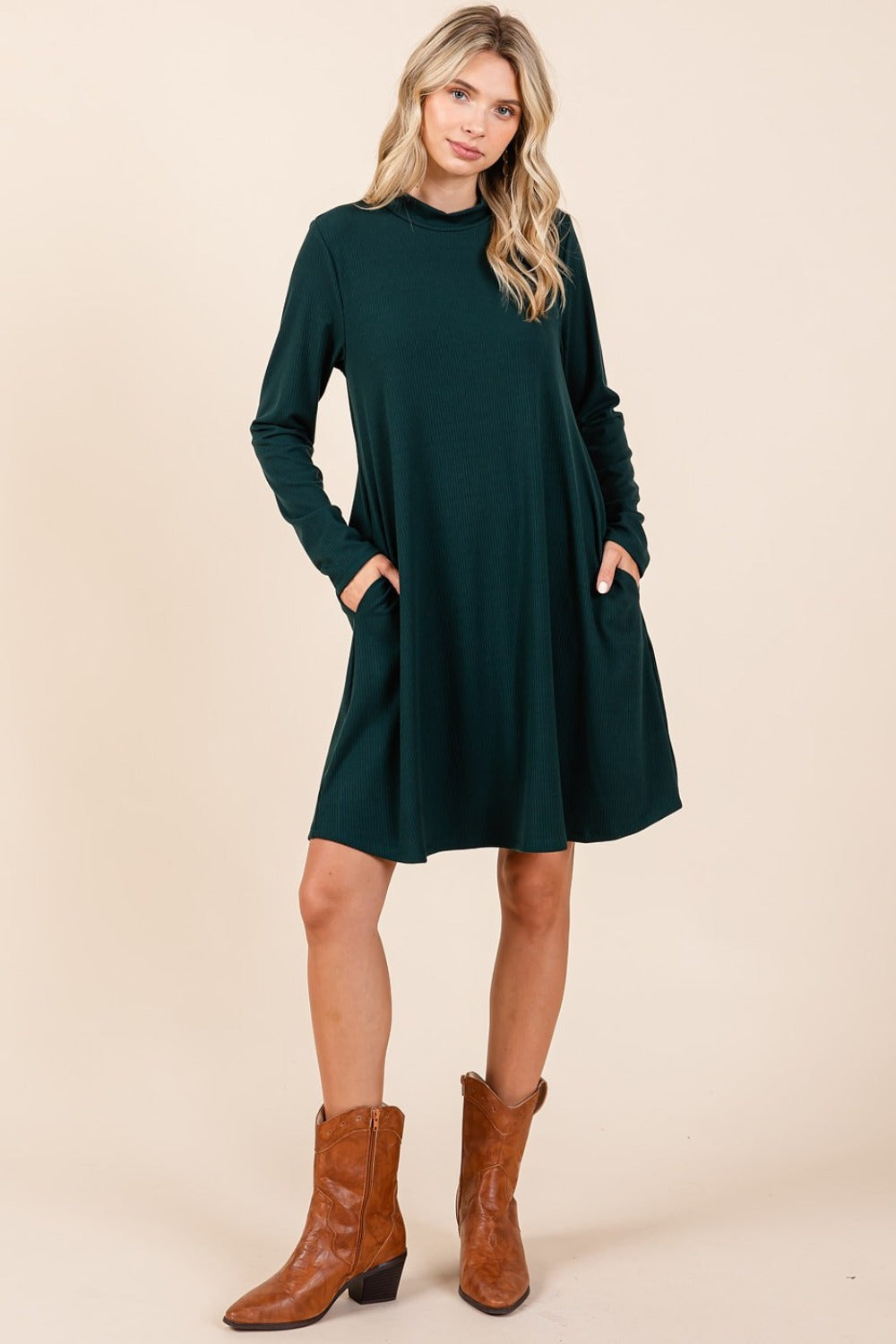 Hunter green mock neck long sleeve dress with pockets, slightly stretchy, featuring a woman styled in brown boots.