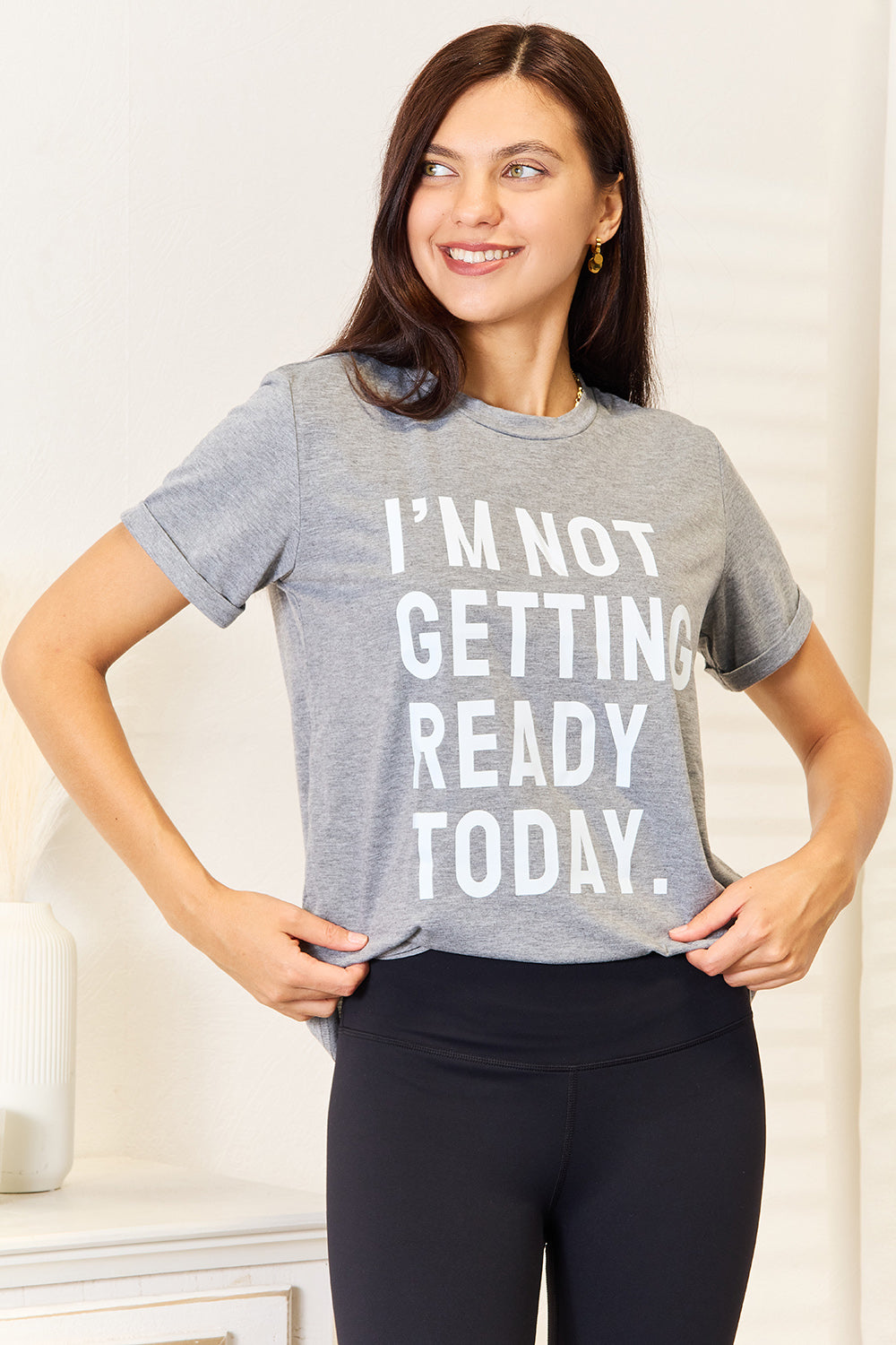 Woman wearing gray "I'm Not Getting Ready Today" graphic T-shirt with black leggings, showcasing casual and comfortable style.