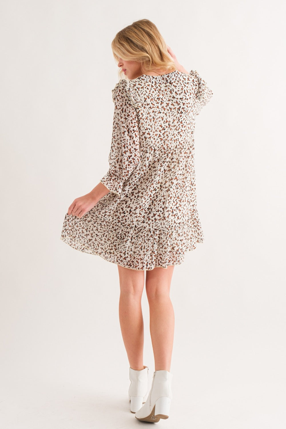 Woman wearing Ivory Leopard Ruffle Hem Woven Mini Dress with ruffled and ruched details, showcasing a slightly stretchy fabric.