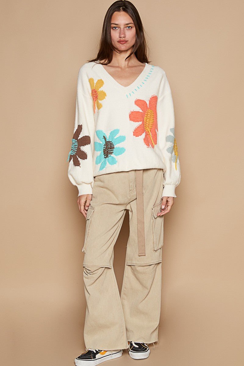 Woman wearing an ivory V-neck long sleeve sweater with colorful flower fringe design, paired with beige cargo pants and sneakers.