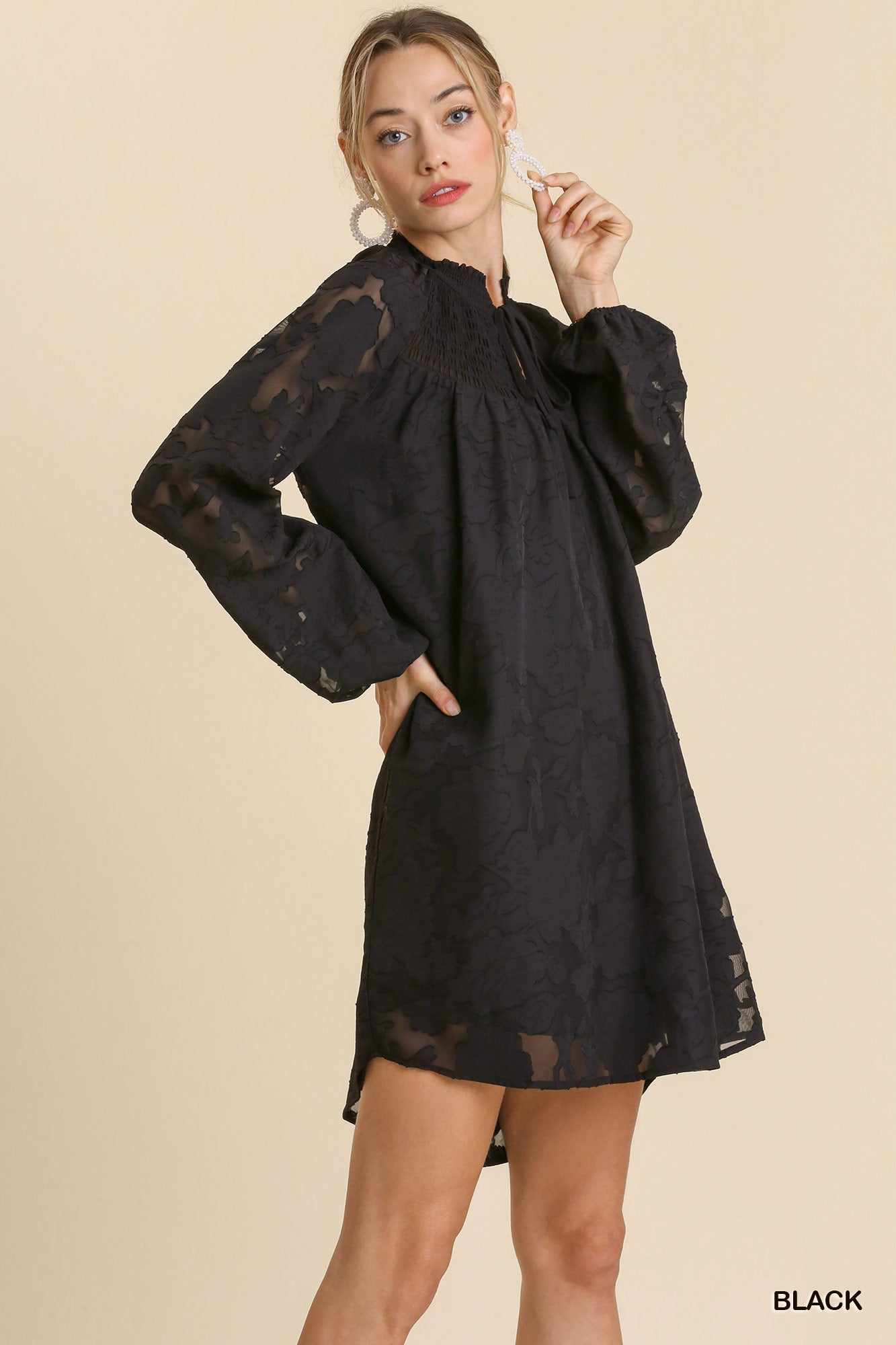 Woman wearing black Jacquard Tie Neck Yoke Dress with long sleeves and smocked detailing.