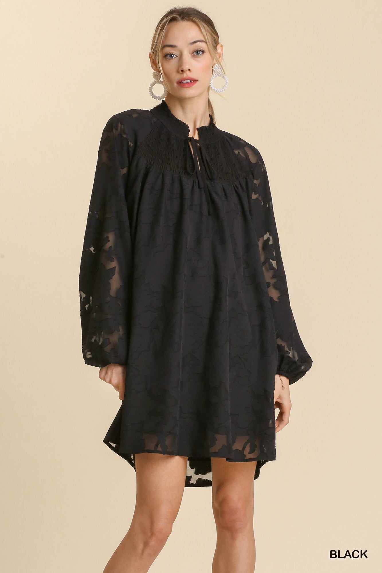 Woman wearing black Jacquard Tie Neck Yoke Dress with raglan sleeves and smocked details, available in sizes S, M, L.