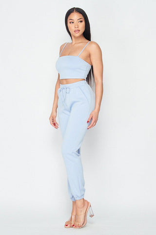 "Woman wearing Keep It Cute Two-Piece Set in light blue, featuring a crop top and jogger pants, made of rayon, polyester, and spandex."
