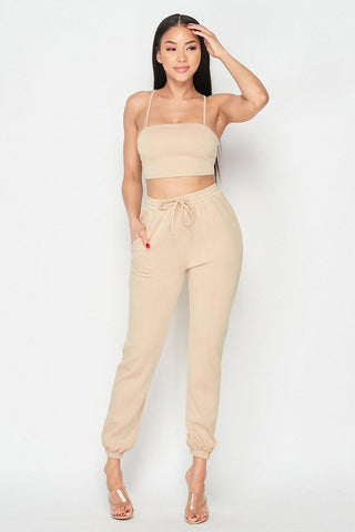 Beige two-piece set featuring a crop top and jogger pants, made of rayon, polyester, and spandex. Fashionable and comfortable outfit.