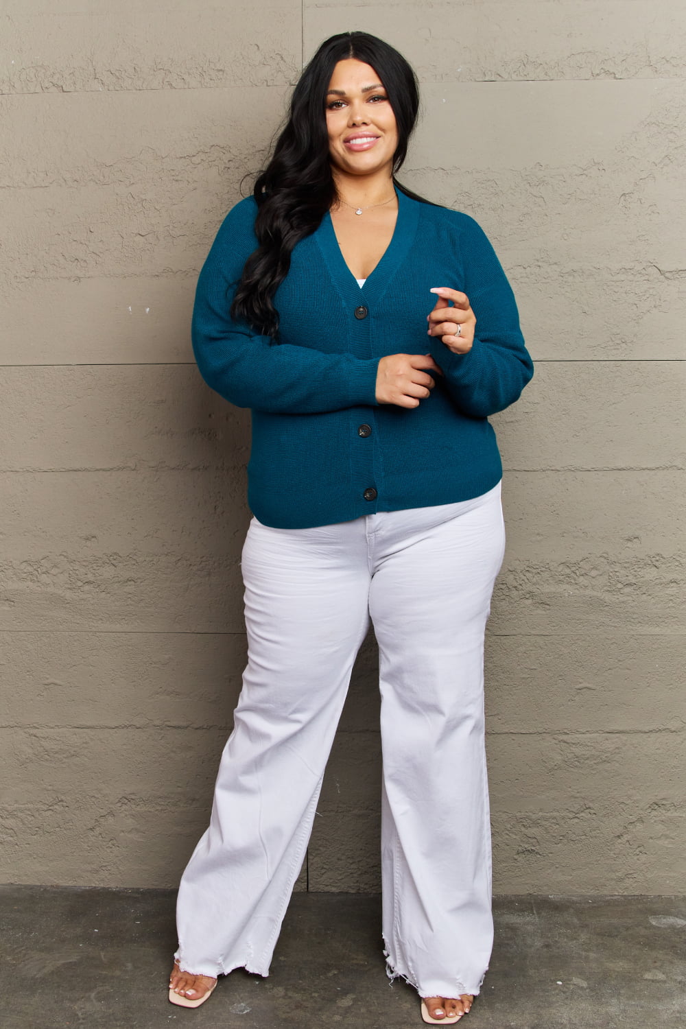 Woman wearing teal button-down V-neck cardigan with ribbed detailing and white pants, showcasing casual outfit style.