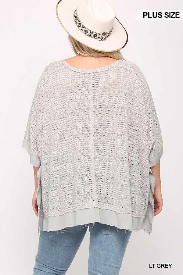 Plus size light grey boxy top with knit and woven texture, poncho sleeve, worn by woman in hat.